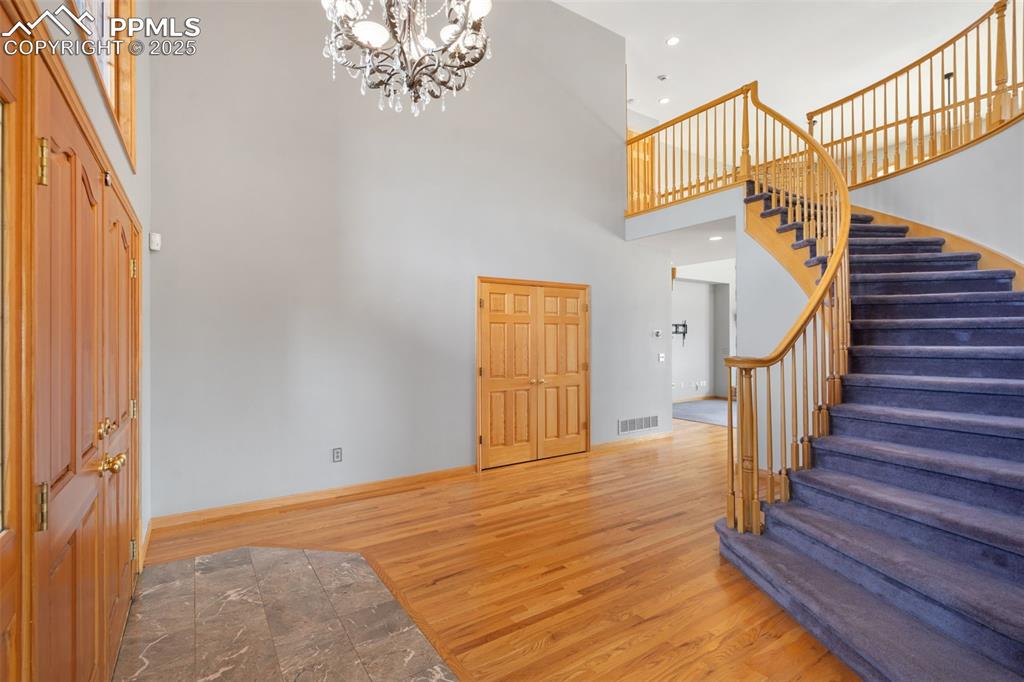 Image 6 of 50: Entryway featuring a high ceiling, stairs, wood finished floors, a chandeli