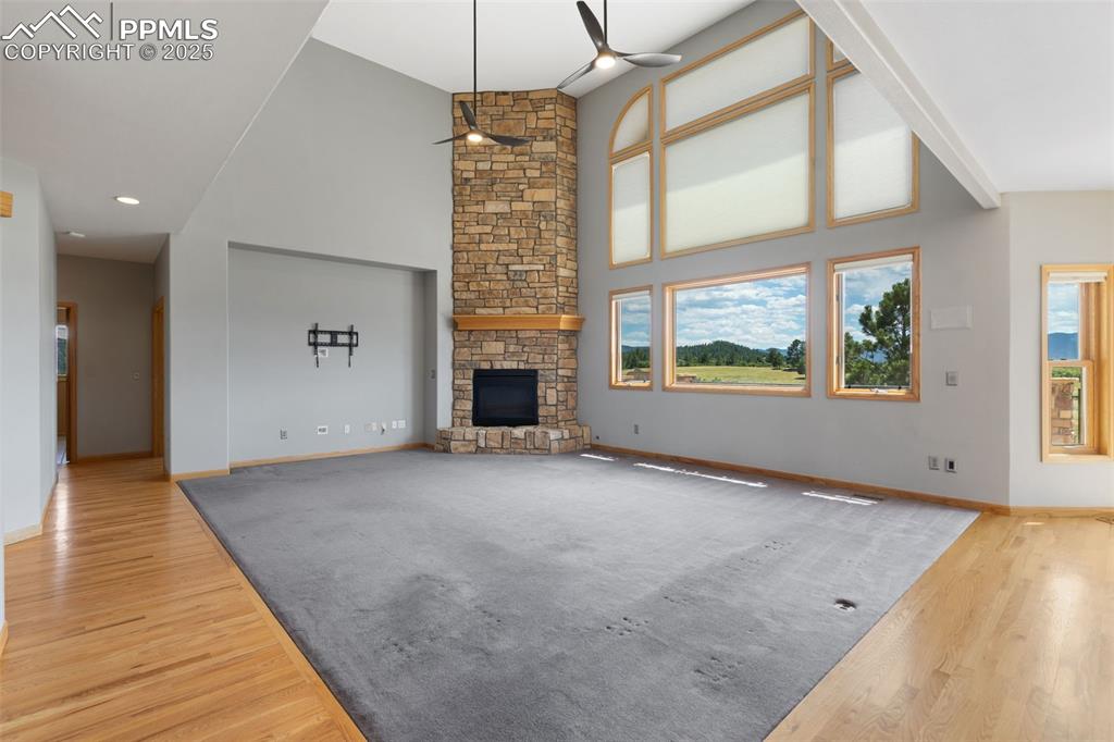 Image 9 of 50: Unfurnished living room with a ceiling fan, wood finished floors, a stone f