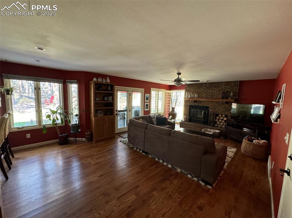 Image 15 of 49: Living area with a fireplace, wood finished floors, ceiling fan, a textured