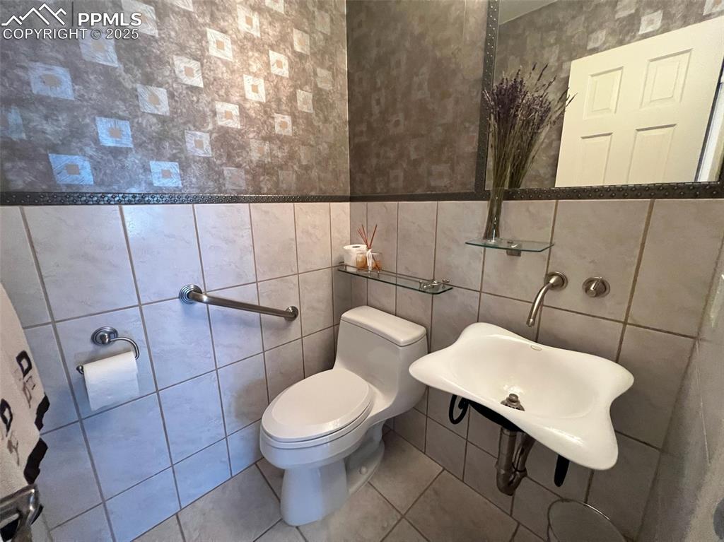 Image 18 of 49: Half bathroom with tile walls, toilet, and tile patterned floors