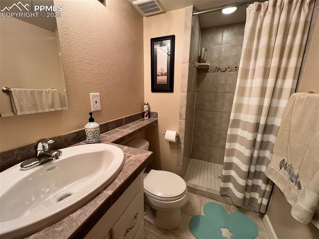 Image 32 of 49: Bathroom featuring a tile shower, toilet, vanity, a textured wall, and tile