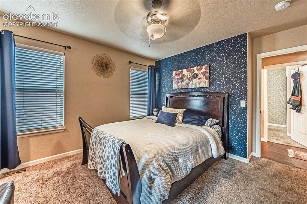 Image 14 of 36: Carpeted bedroom with a textured ceiling, a ceiling fan, and wallpapered wa