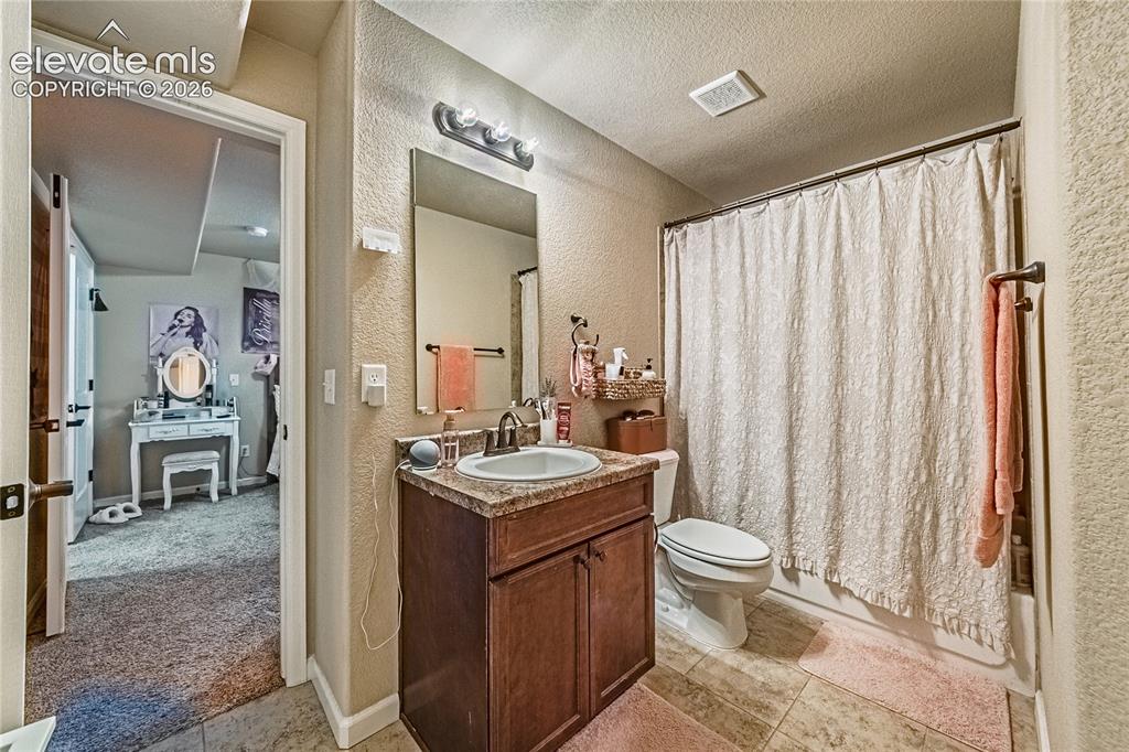 Image 28 of 36: Full bath with a textured wall, vanity, shower / tub combo, a textured ceil