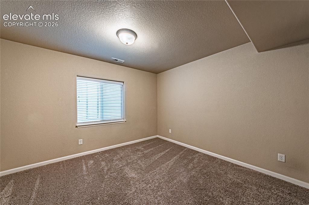 Image 29 of 36: Bedroom featuring a textured wall, dark colored carpet, and a textured ceil