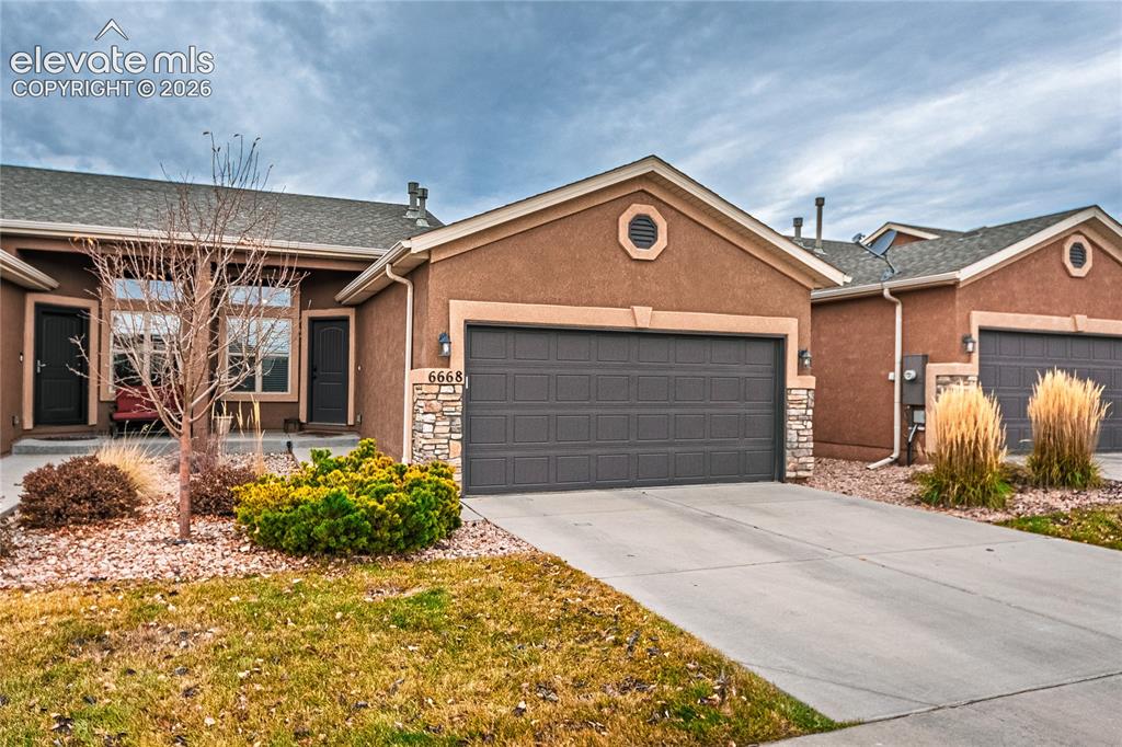 Image 34 of 36: Ranch-style home featuring a garage, stucco siding, driveway, and stone sid
