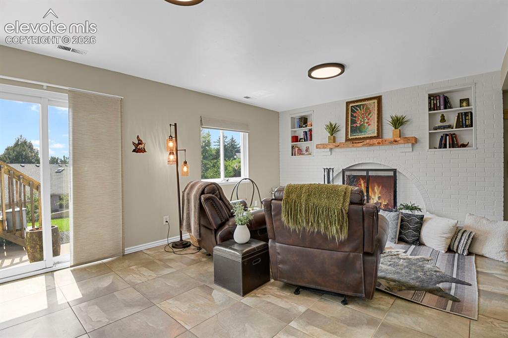 Image 22 of 38: Tiled flooring and a brick fireplace with a wood mantle