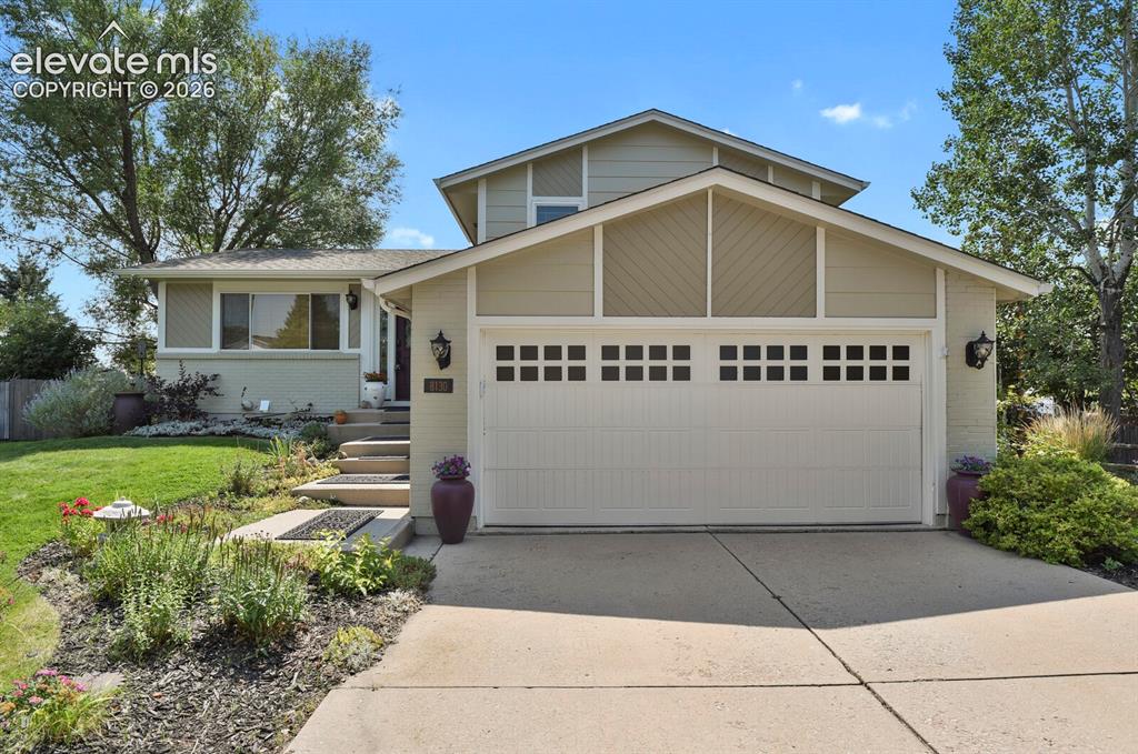 Image 3 of 38: Two-car garage with divided light windows, concrete driveway, and landscape