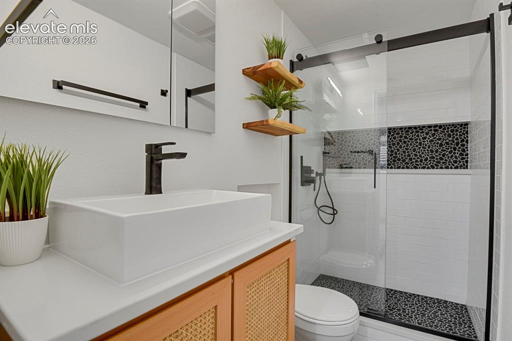 Image 31 of 38: Modern bathroom featuring a glass-enclosed shower, black pebble tile shower