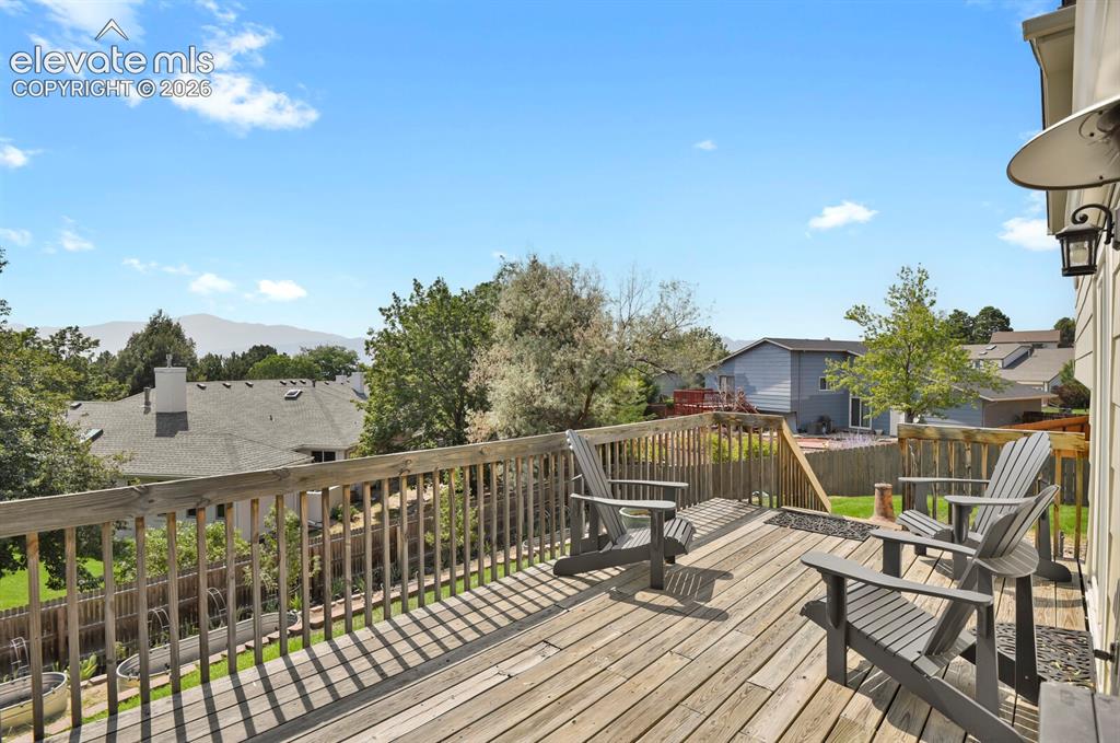Image 35 of 38: Expansive wood deck with a mountain backdrop, surrounded by mature trees