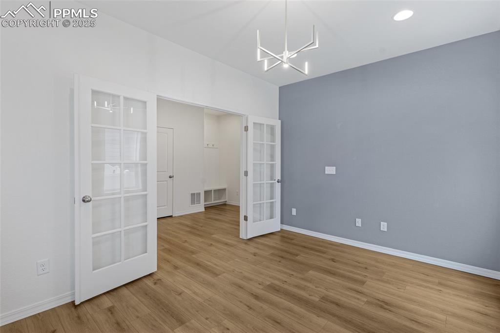Image 11 of 50: Empty room featuring french doors, a chandelier, wood finished floors, and