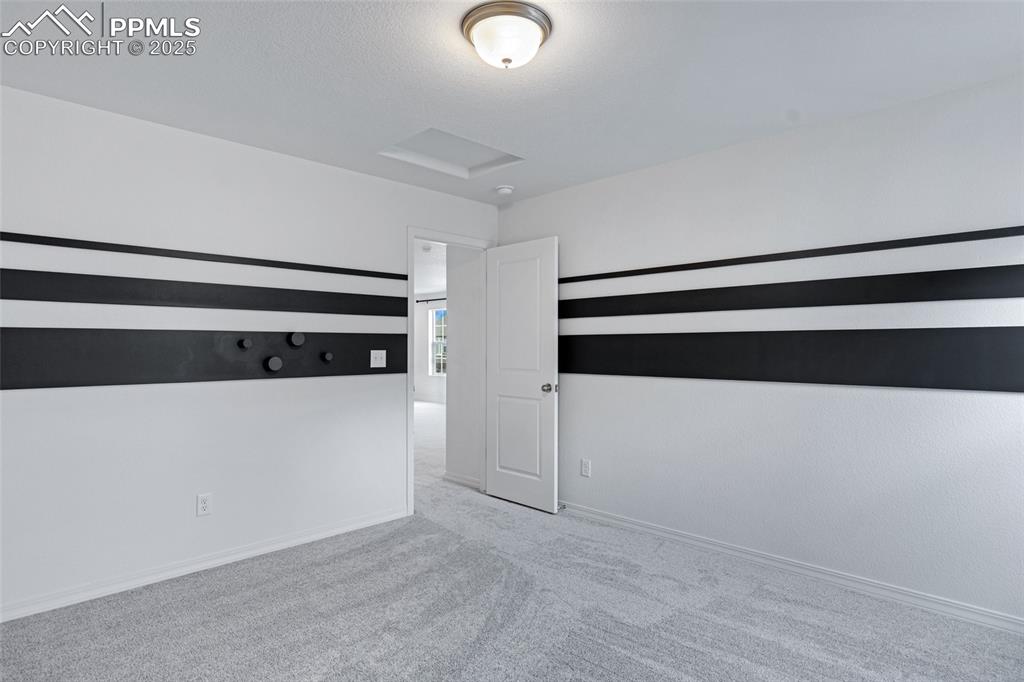 Image 28 of 50: Carpeted empty room with attic access and baseboards
