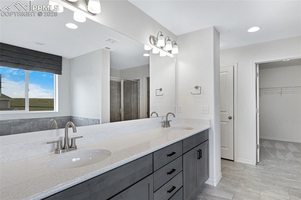 Image 33 of 50: Bathroom with double vanity, a stall shower, a walk in closet, recessed lig
