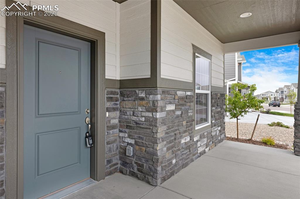 Image 7 of 50: Property entrance with covered porch and stone siding