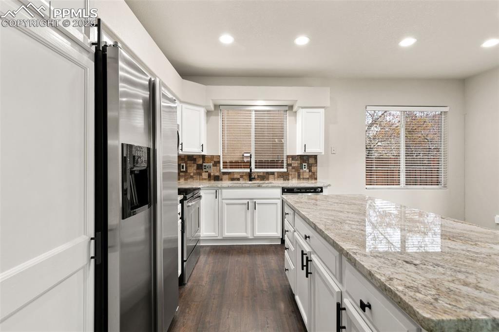Image 12 of 27: Kitchen with backsplash, white cabinets, light stone counters, stainless st