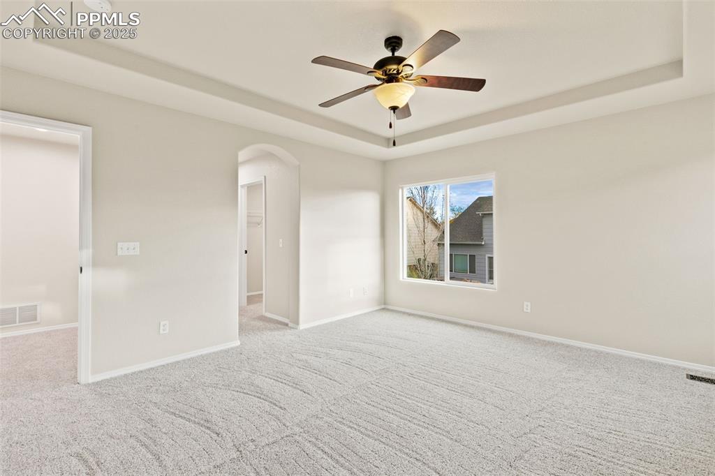 Image 16 of 27: Carpeted empty room with a tray ceiling, arched walkways, and a ceiling fan