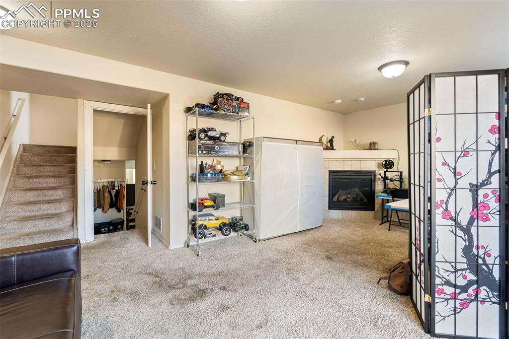 Image 39 of 46: Below grade area with a tile fireplace, light carpet, a textured ceiling, a