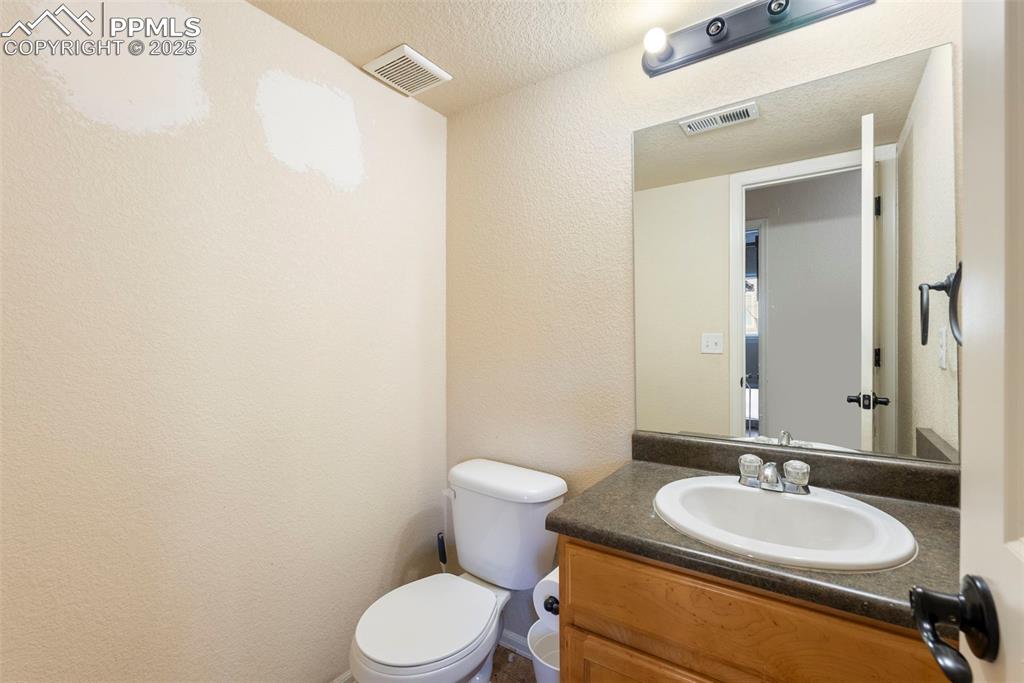 Image 41 of 46: Half bathroom with a textured wall, vanity, and a textured ceiling