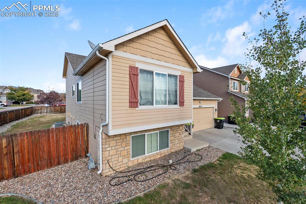 Image 6 of 46: View of side of home featuring driveway, stone siding, and a shingled roof