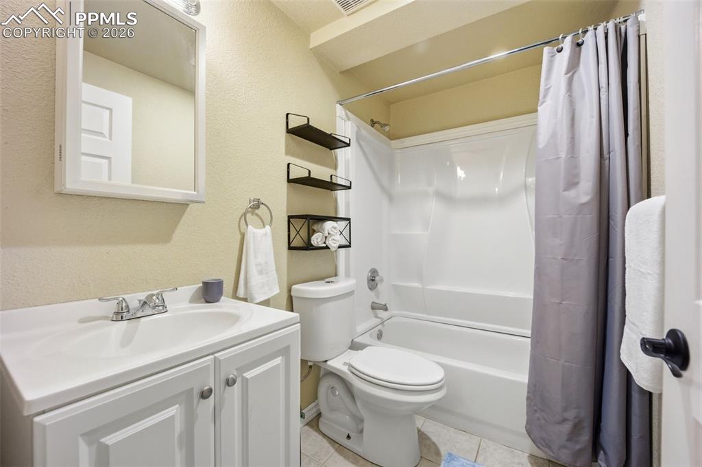 Image 31 of 46: Full bathroom featuring a textured wall, vanity, shower / tub combo, and li