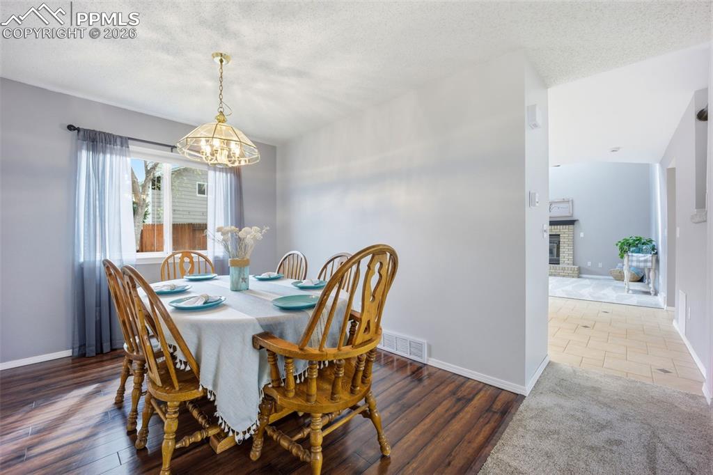 Image 7 of 46: Dining space featuring a fireplace, wood finished floors, and suspended lig