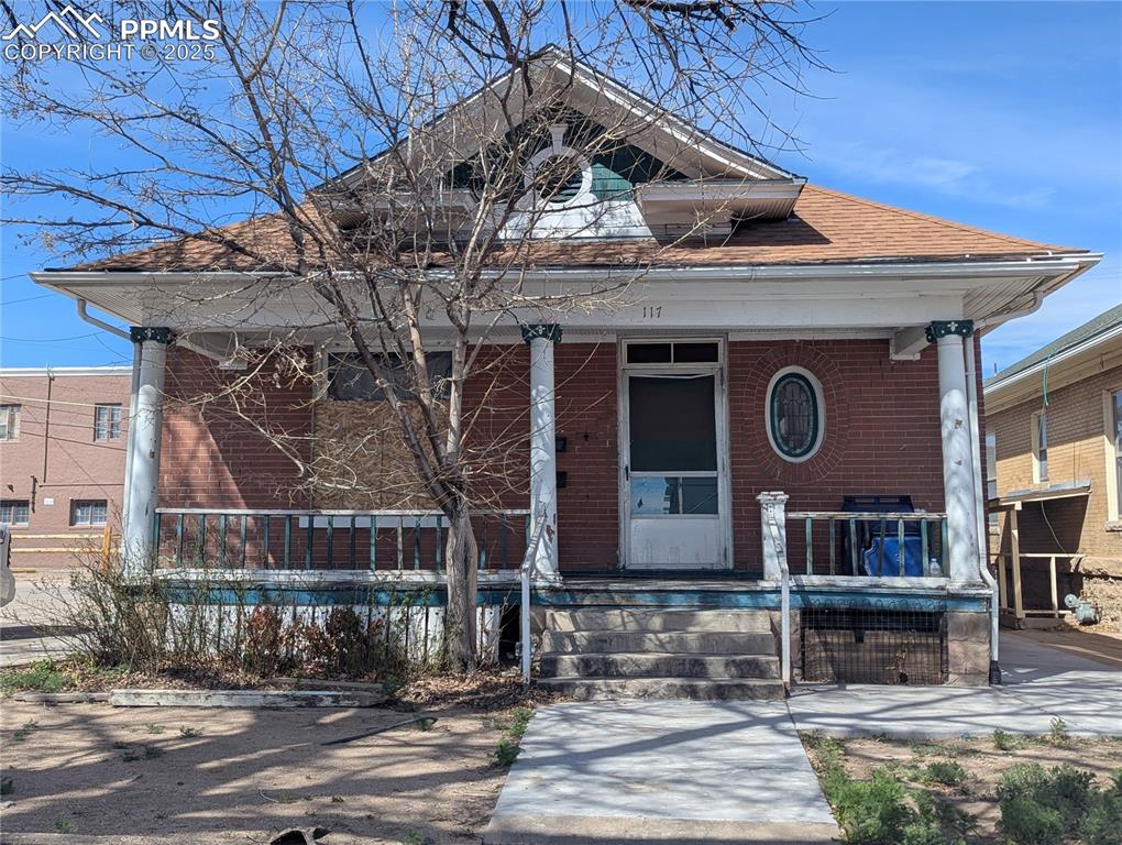 Caption: View of front of home with brick siding, covered porch, and a shingled roof