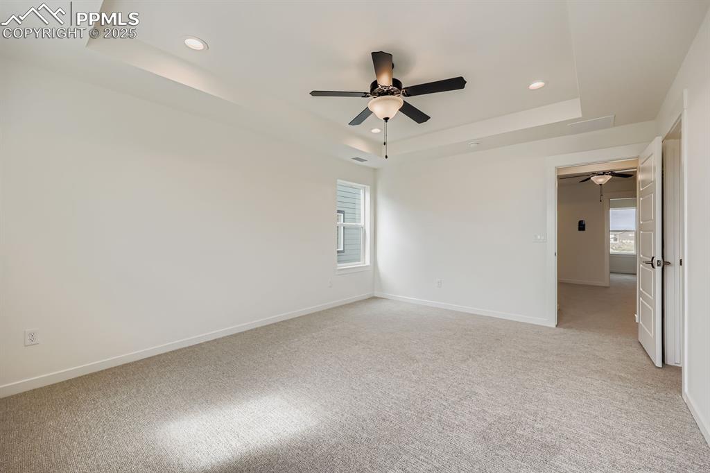 Image 16 of 28: Unfurnished room with light colored carpet, ceiling fan, a tray ceiling, an