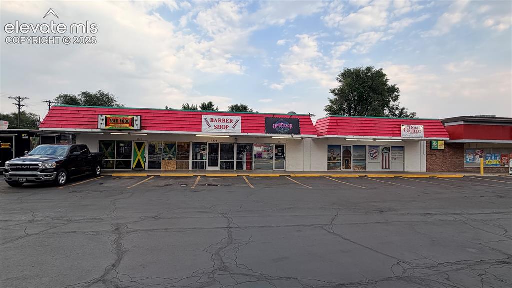 Caption: Commercial building featuring multiple storefronts, a red shingled roof, and an asphalt parking lot