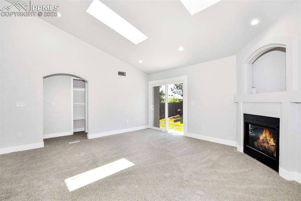 Image 30 of 44: Unfurnished living room with arched walkways, carpet, a glass covered firep