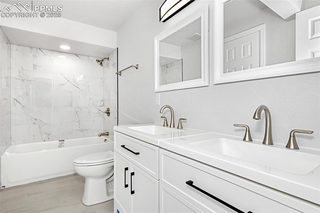 Image 42 of 44: Bathroom featuring double vanity, washtub / shower combination, and wood fi