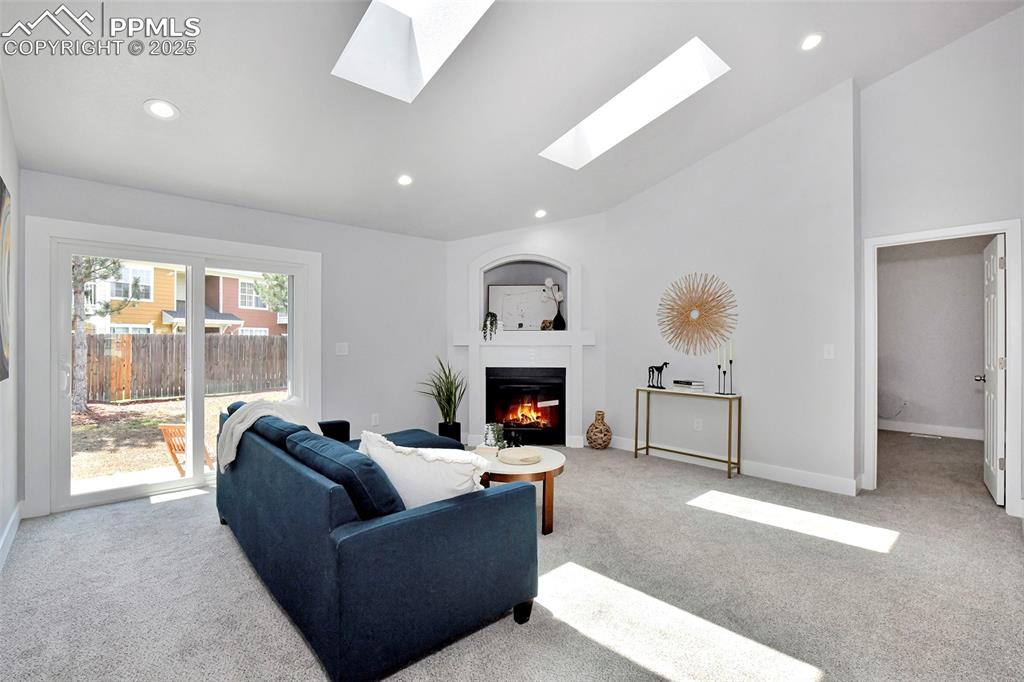 Image 8 of 44: Living area with a glass covered fireplace, light carpet, recessed lighting
