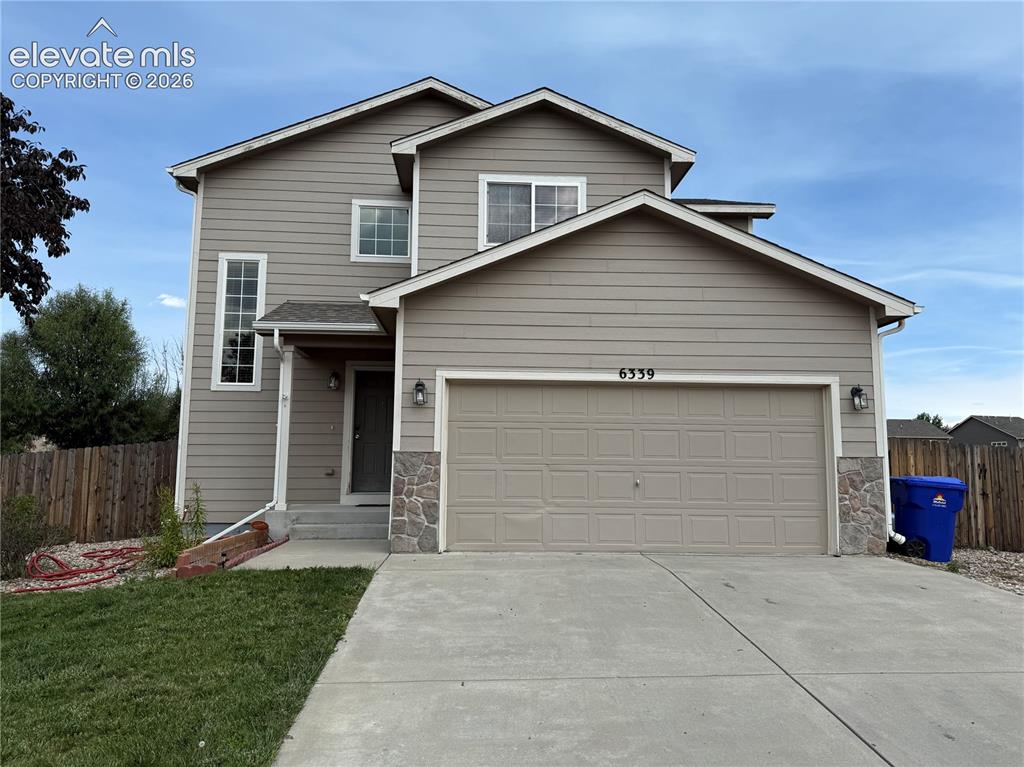 Caption: Two-story exterior with neutral siding, an attached garage, a covered front entry, and stacked stone