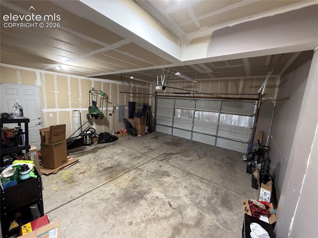 Image 14 of 16: Attached garage with a roll-up door, exposed ceiling joists, and a side ent