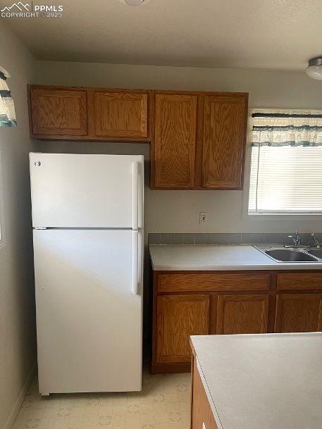 Image 5 of 5: Kitchen featuring brown cabinets, light countertops, freestanding refrigera