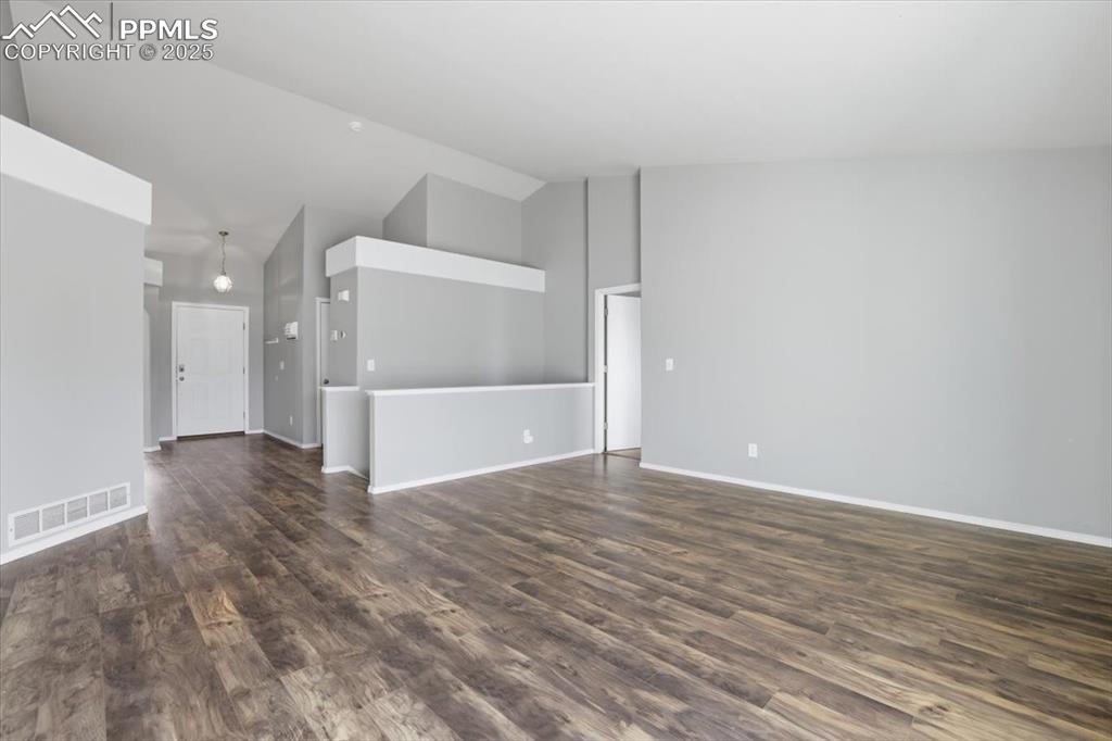 Image 15 of 43: Unfurnished living room with dark wood-style flooring and high vaulted ceil