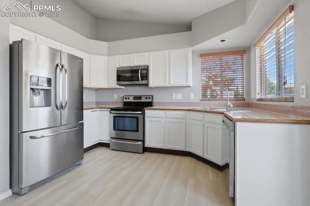 Image 4 of 43: Kitchen with appliances with stainless steel finishes, tile counters, and w