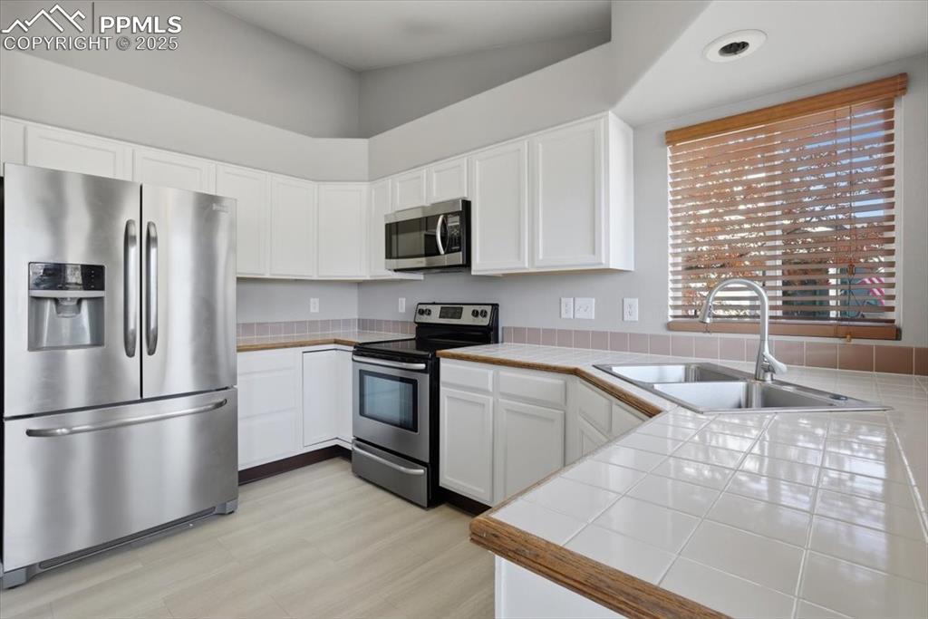 Image 5 of 43: Kitchen featuring tile countertops, appliances with stainless steel finishe