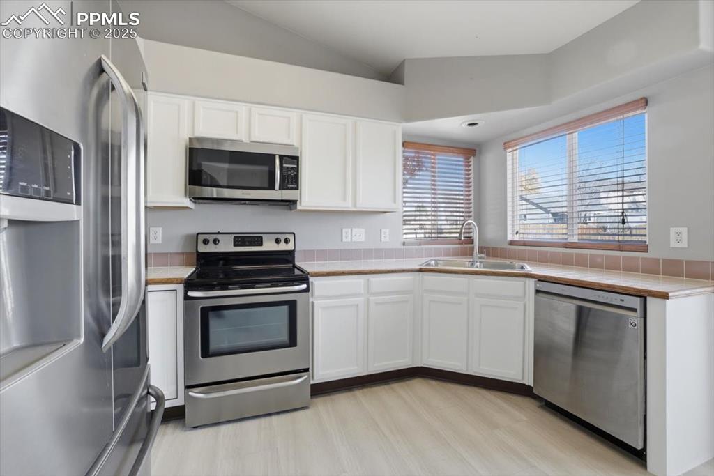 Image 6 of 43: Kitchen featuring stainless steel appliances, tile countertops, white cabin