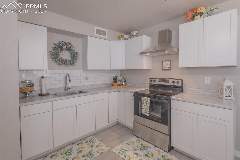 Image 6 of 21: Kitchen with electric stove, wall chimney range hood, light countertops, an