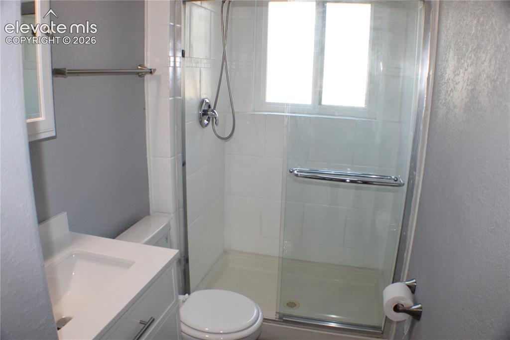 Image 20 of 28: Glass-enclosed shower with white tiled walls, a window, and a built-in show