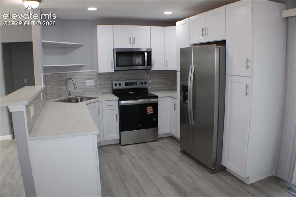 Image 7 of 28: Modern kitchen featuring white cabinetry, light countertops, wood-finish fl