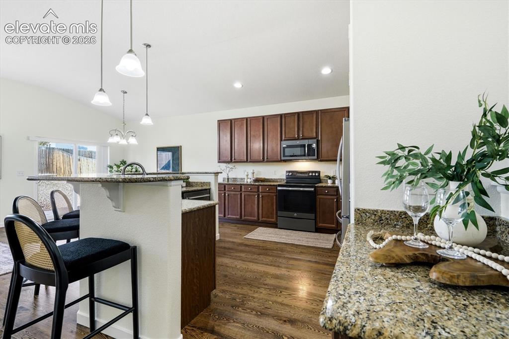 Image 7 of 45: Kitchen featuring wood-finish flooring, dark wood cabinetry, granite counte