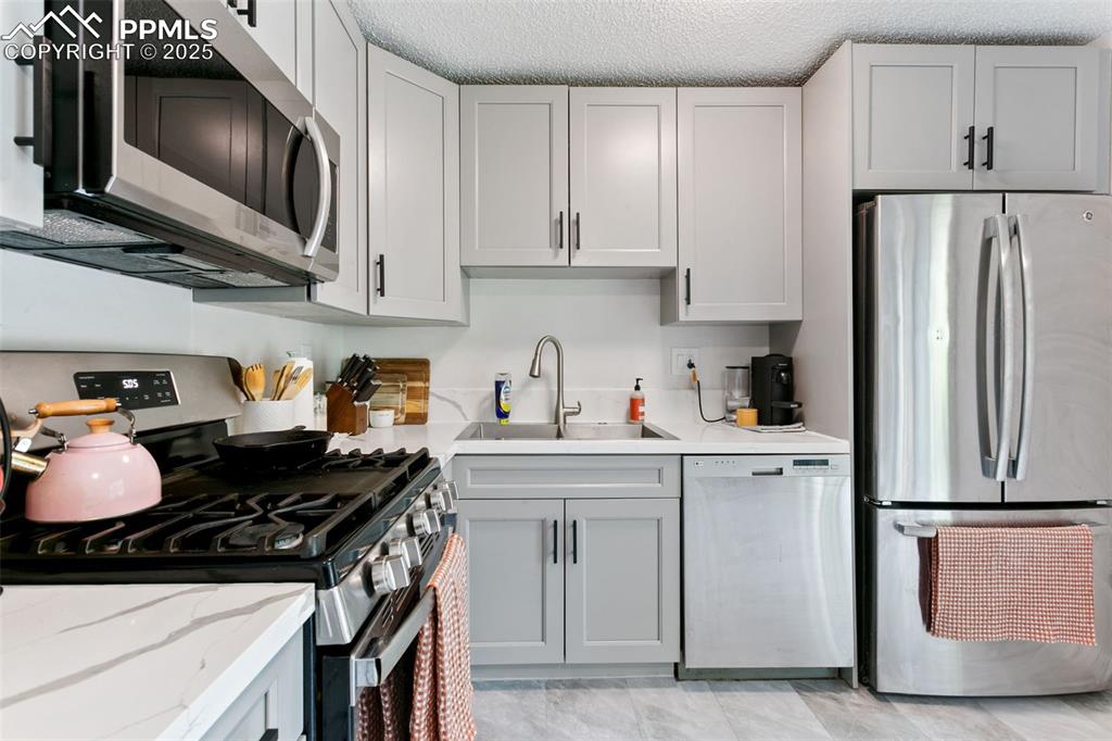 Image 12 of 28: Kitchen with appliances with stainless steel finishes, gray cabinetry, ligh
