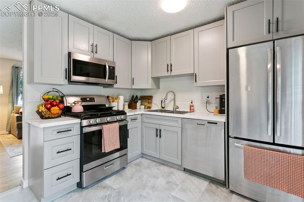 Image 14 of 28: Kitchen with stainless steel appliances, a textured ceiling, gray cabinetry