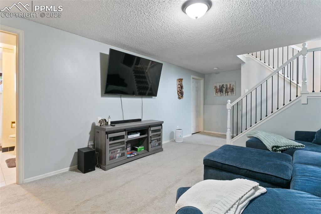 Image 18 of 28: Carpeted living room featuring a textured ceiling and stairway