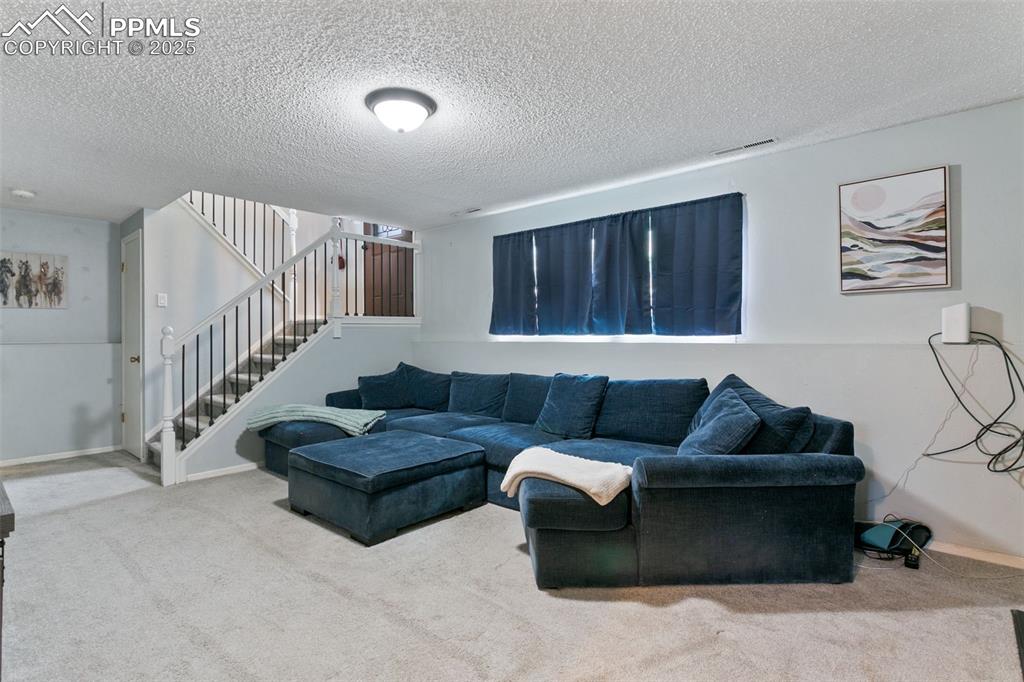Image 19 of 28: Carpeted living area with a textured ceiling and stairs
