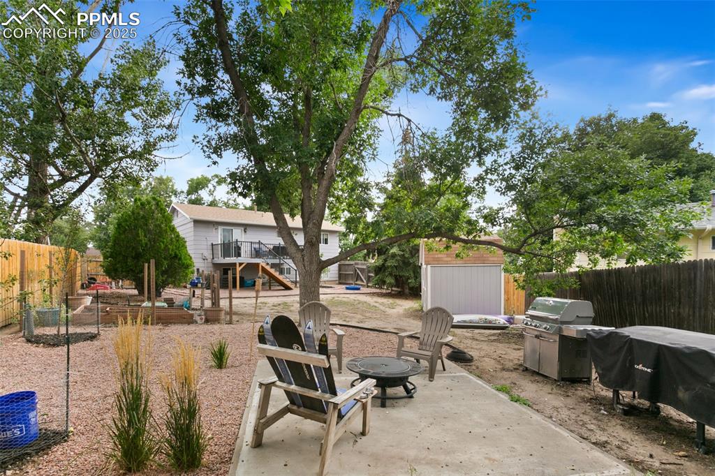 Image 4 of 28: Fenced backyard with a patio area, a fire pit, a storage unit, a grill, and