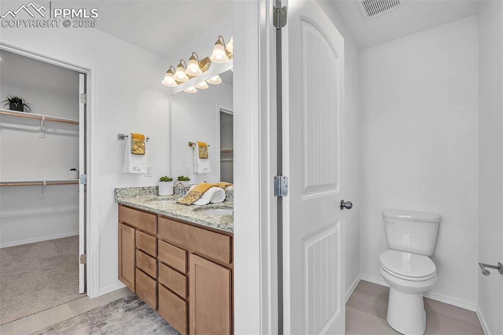 Image 24 of 33: Full bathroom featuring toilet, vanity, a spacious closet, tile patterned f