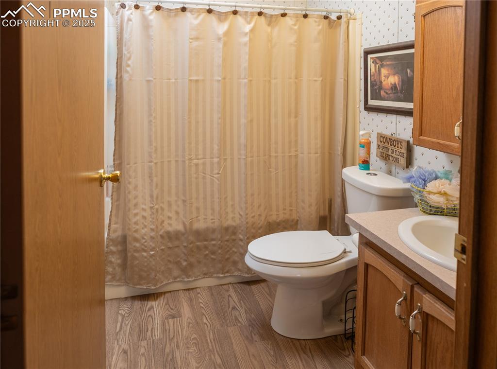 Image 17 of 50: Bathroom featuring wallpapered walls, wood finished floors, and vanity