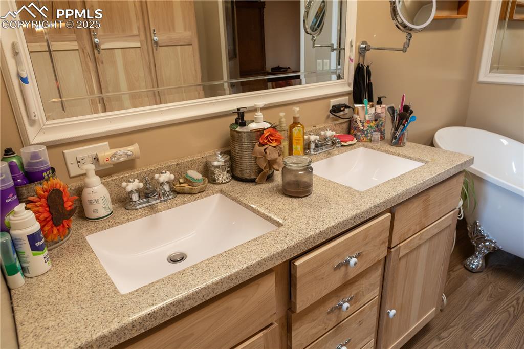 Image 22 of 50: Bathroom featuring double vanity, a freestanding tub, and wood finished flo