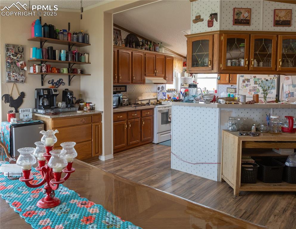 Image 31 of 50: Kitchen featuring electric stove, brown cabinets, wood finished floors, orn